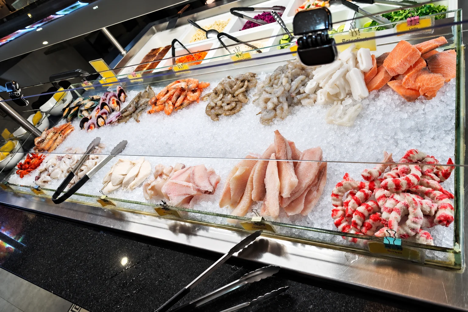 Seafood on ice at the buffet: prawns, salmon, squid, fish fillets and surimi, tongs in front.