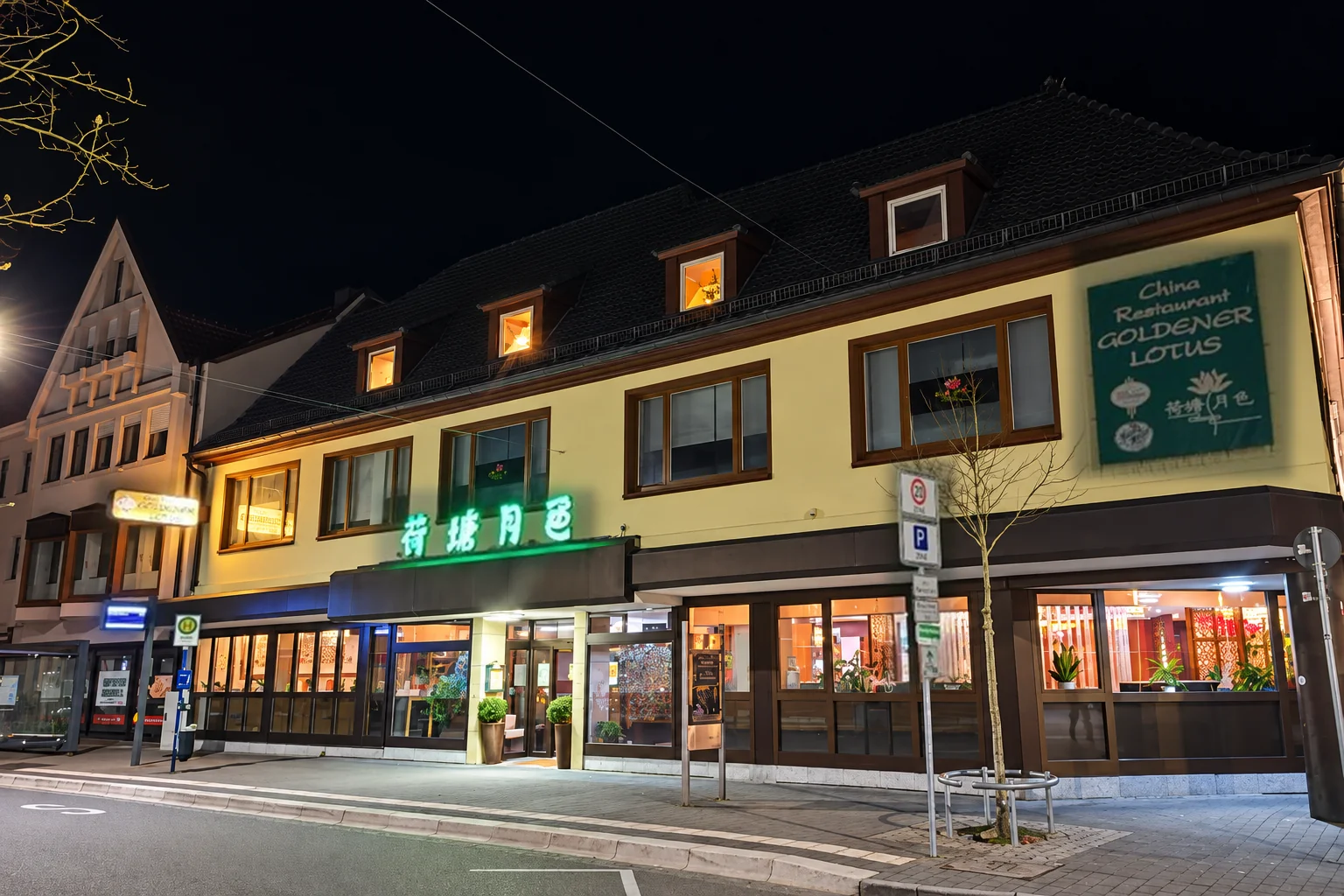 The Goldener Lotus façade in the evening: a yellow building, green neon lettering above the entrance, a “China Restaurant Goldener Lotus” sign, lit windows.